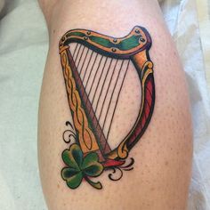 a tattoo on the leg of a woman with a harp and shamrocks around it