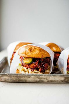 three sandwiches are wrapped in white paper on a metal tray, ready to be eaten