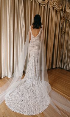 a woman wearing a wedding dress and veil standing in front of a curtained wall