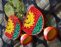 two red, yellow and green earrings sitting on top of a piece of fabric next to each other