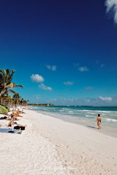 people are walking on the beach near the water and palm trees in the background,