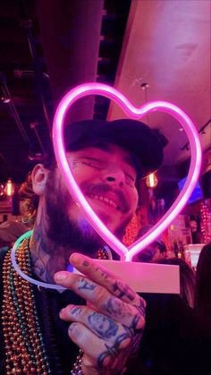 a man holding up a heart shaped neon sign in front of his face with beads all around him