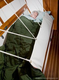 an older man laying in a bed with green sheets on top of it and tied to the wall