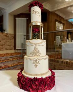 a three tiered white wedding cake with red roses on the bottom and gold trimmings