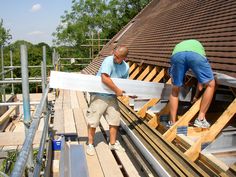 two men are working on the roof of a house that is being built with wood planks