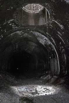 the inside of a dark tunnel with light coming from it's top and floor