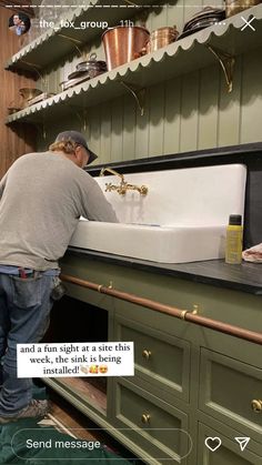 a man fixing a sink in a kitchen with green cupboards and shelves above it