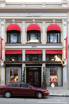 a red car parked in front of a building with christmas decorations on it's windows