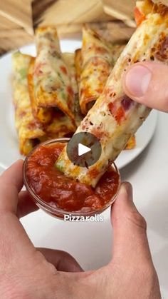 a person holding a piece of pizza in their hand and dipping it into a small bowl