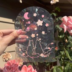 a person holding up a piece of glass with pink flowers in the background