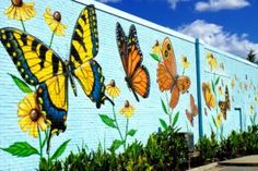 a painted mural on the side of a building with yellow and black butterflies flying over flowers