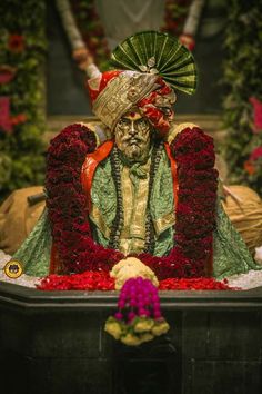 a statue is sitting in the middle of red flowers and greenery with a fan on it's head