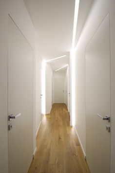 an empty hallway with white walls and wooden floors is lit by recessed lighting on either side