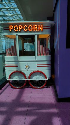 an old fashioned popcorn cart on display in a building with purple walls and pink flooring