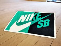 a green and black rug with the word nike sb on it sitting on a wooden floor