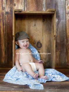 a baby sitting in a wooden crate with a blanket on it's lap and smiling at the camera