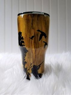 a wooden cup with birds painted on the side and black paint, sitting on a fluffy white surface