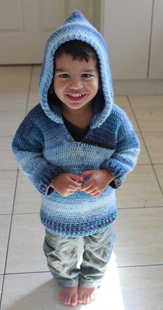 a young boy wearing a blue knitted hoodie and smiling at the camera with his hands in his pockets