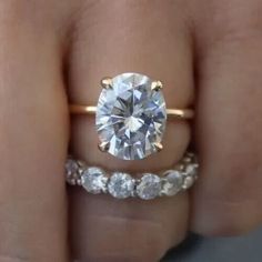 a woman's hand holding an engagement ring with a diamond in the center and two wedding bands around it