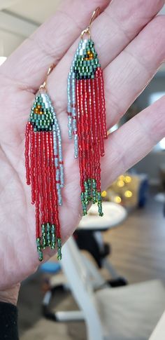 the hand is holding two red and green beaded earrings