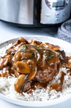 a white plate topped with rice and meat covered in gravy next to an instant pressure cooker