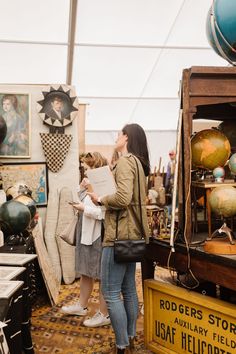 two women looking at art on display in an open air market area with globes and other items