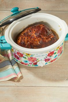 a slow cooker filled with food on top of a wooden table next to utensils