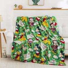 a green mickey mouse christmas blanket on a couch in a living room with white furniture