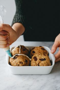 a person is spreading icing on some cookies in a white bowl with other muffins