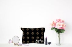 a black and gold make up bag sitting on top of a table next to a vase with pink flowers