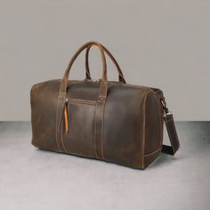 a brown leather duffel bag sitting on top of a gray floor next to a wall