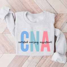 a grey sweatshirt with the word cna on it sitting on top of a wooden floor