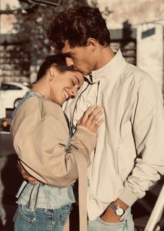 a man and woman standing next to each other in front of a street sign with their arms around each other