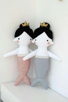 two dolls are standing next to each other on a white shelf in front of a clock