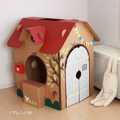 a cardboard house with a red roof and two white rabbits sitting in front of it