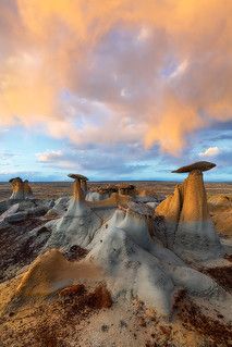 the desert is covered in white and brown sand, under a colorful cloud filled sky