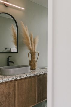 a bathroom with a sink, mirror and vase on the counter top in front of it