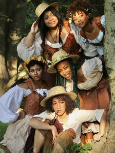 four young women dressed in period clothing posing for a photo together with trees and grass behind them