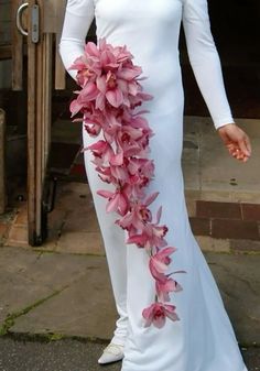 a woman wearing a white dress with pink flowers on the side and long sleeves is standing in front of a door