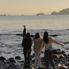 three women are standing on rocks near the water with their arms in the air and one is raising her hands