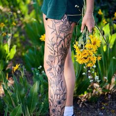 a person with tattoos on their legs holding flowers in front of some grass and yellow flowers