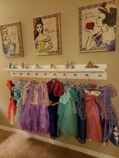 there are many princess dresses hanging on the rack in front of the pictures and paintings