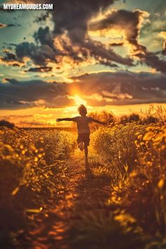 a person walking down a dirt road with their arms outstretched in front of the sun