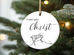 a ceramic ornament hanging from a christmas tree with the words, come unto christ