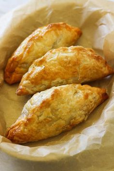 three pastries sitting on top of a piece of wax paper in a brown bowl