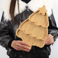 a woman in black jacket holding wooden tray with christmas tree design on the bottom and white fur collar