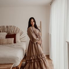 a woman standing in front of a bed wearing a long brown dress with tiered ruffles