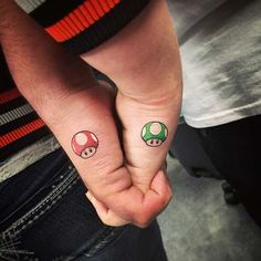 two people holding hands with small tattoos on their thumb and fingers, one has a mushroom tattooed on the other