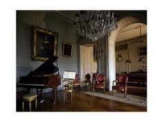 a grand piano sitting in the middle of a room with chandelier and chairs