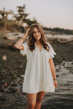 a woman standing on the beach with her hands in her hair and wearing a white dress